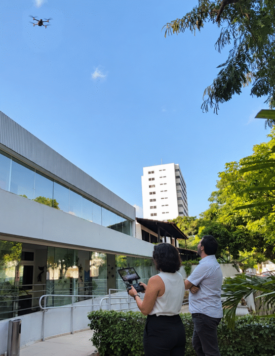 mulher e homem em área externa de uma edificação, pilotado um drone